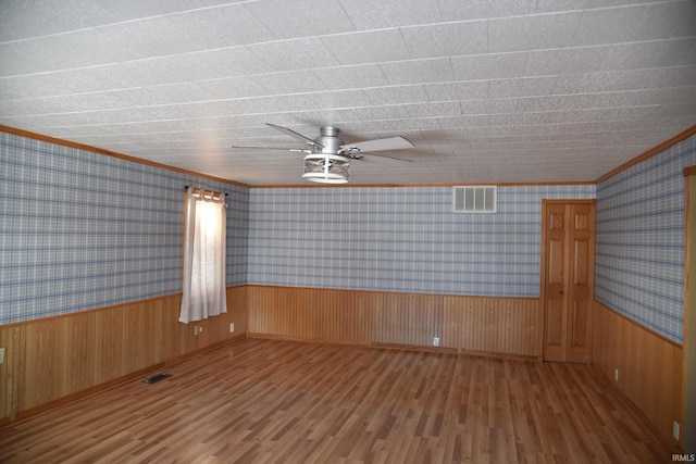 spare room featuring ornamental molding, hardwood / wood-style floors, ceiling fan, and wood walls