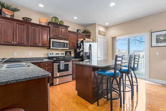 kitchen with sink, a kitchen island, stainless steel appliances, light hardwood / wood-style floors, and a kitchen bar