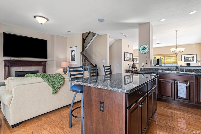 kitchen with dark brown cabinetry, a breakfast bar, sink, decorative light fixtures, and a tile fireplace