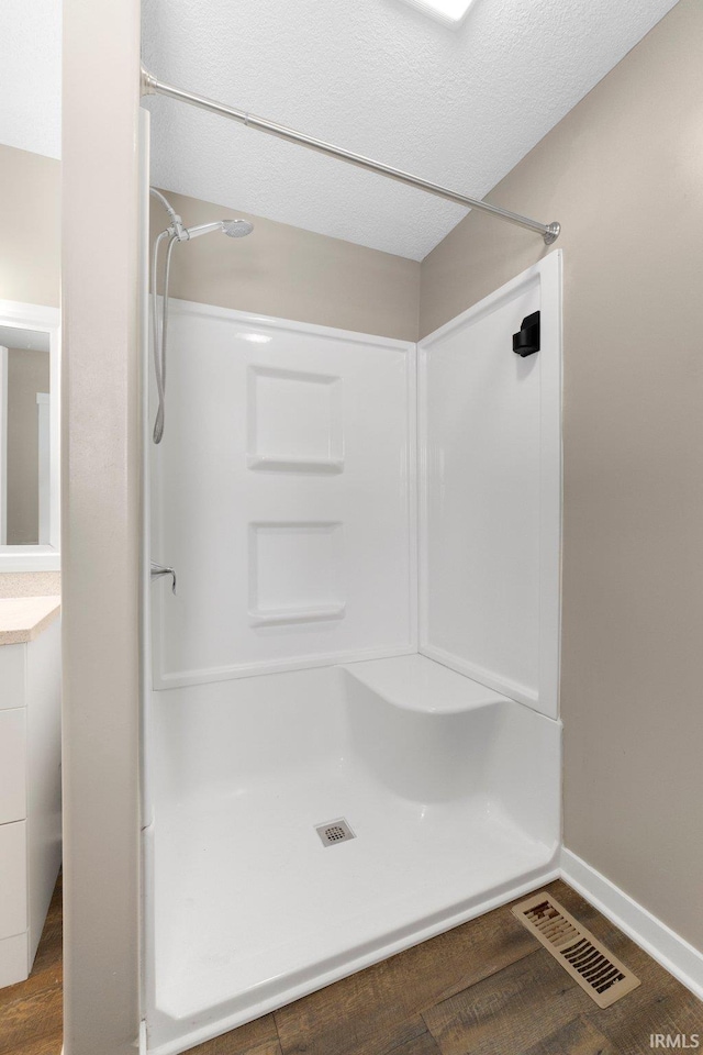 bathroom featuring hardwood / wood-style flooring, a shower, and a textured ceiling