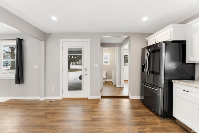 kitchen with stainless steel refrigerator with ice dispenser, a healthy amount of sunlight, dark wood-type flooring, and white cabinets