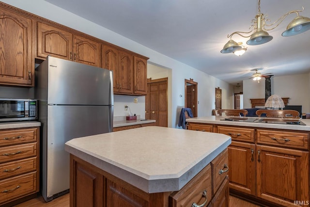 kitchen featuring light wood-type flooring, decorative light fixtures, a kitchen island, and appliances with stainless steel finishes