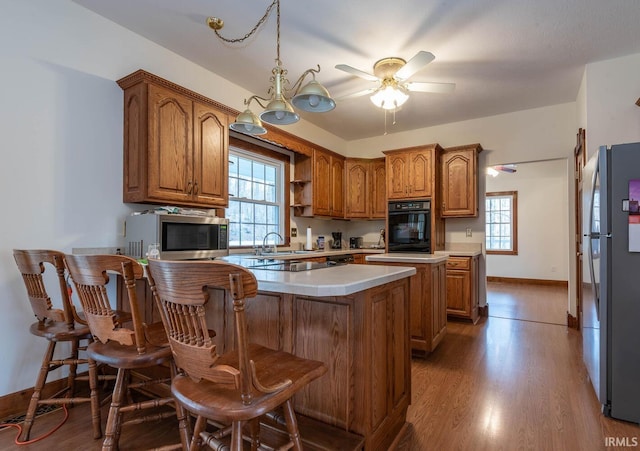 kitchen featuring a breakfast bar area, wood-type flooring, decorative light fixtures, ceiling fan, and stainless steel appliances