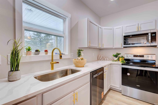 kitchen with sink, appliances with stainless steel finishes, white cabinetry, light stone countertops, and light hardwood / wood-style floors