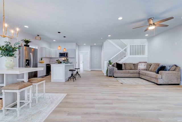 living room with ceiling fan with notable chandelier and light hardwood / wood-style flooring