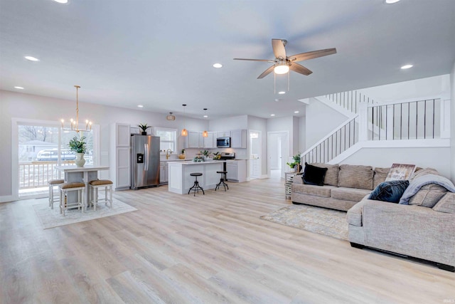 living room with ceiling fan with notable chandelier and light wood-type flooring