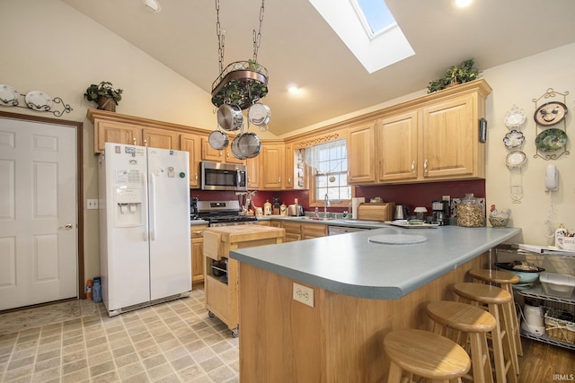 kitchen featuring lofted ceiling with skylight, appliances with stainless steel finishes, light brown cabinetry, sink, and kitchen peninsula