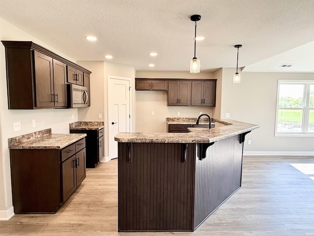 2360 Serenity Ct, Auburn, IN 46706 - kitchen with stainless steel microwave, light wood-style flooring, dark brown cabinets, baseboards, and a breakfast bar