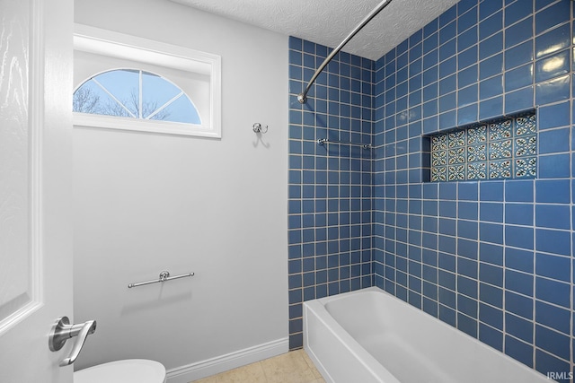 bathroom featuring tiled shower / bath, tile patterned floors, a textured ceiling, and toilet