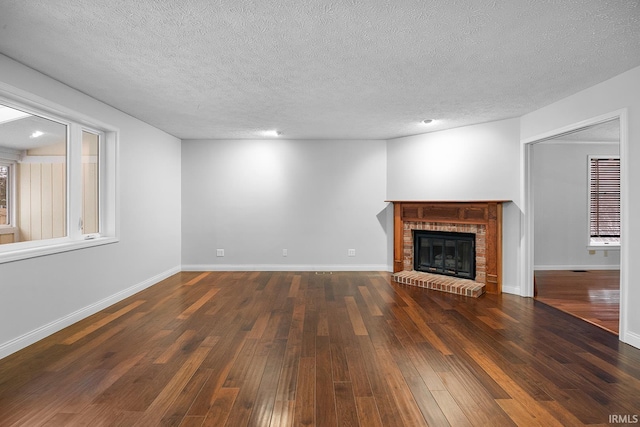 unfurnished living room featuring a brick fireplace, dark hardwood / wood-style floors, a wealth of natural light, and a textured ceiling