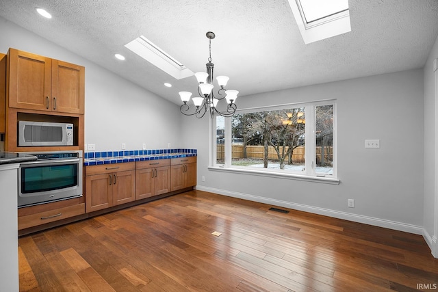 kitchen with pendant lighting, dark wood-type flooring, lofted ceiling with skylight, stainless steel appliances, and a textured ceiling