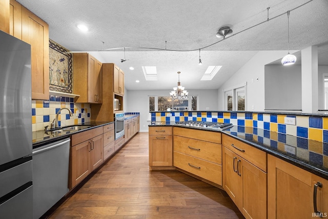 kitchen featuring sink, appliances with stainless steel finishes, hanging light fixtures, a textured ceiling, and decorative backsplash