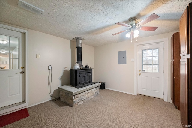 living room featuring a textured ceiling, light colored carpet, electric panel, and a wood stove