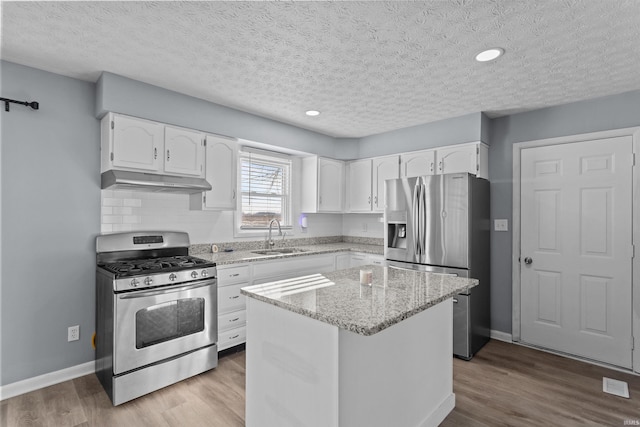 kitchen featuring sink, stainless steel appliances, a center island, light stone countertops, and white cabinets