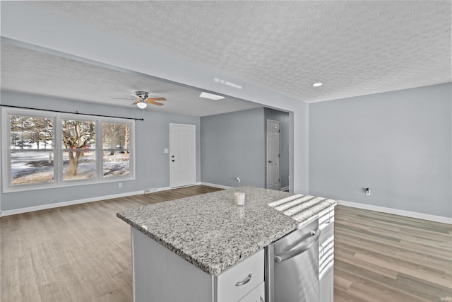 kitchen featuring light hardwood / wood-style flooring, a center island, light stone counters, a textured ceiling, and white cabinets