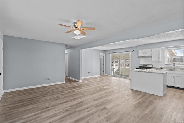 kitchen with stainless steel stove, light hardwood / wood-style flooring, ceiling fan, light stone counters, and white cabinets