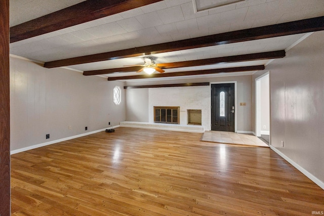 unfurnished living room with a brick fireplace, beamed ceiling, light hardwood / wood-style floors, and ceiling fan