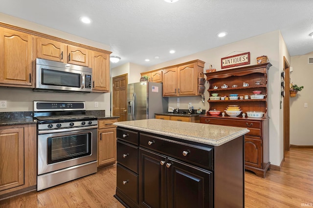 kitchen with a kitchen island, light stone counters, dark brown cabinetry, stainless steel appliances, and light hardwood / wood-style floors