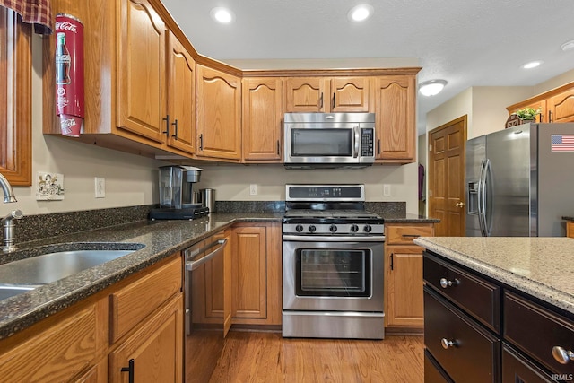 kitchen with stone counters, appliances with stainless steel finishes, sink, and light wood-type flooring