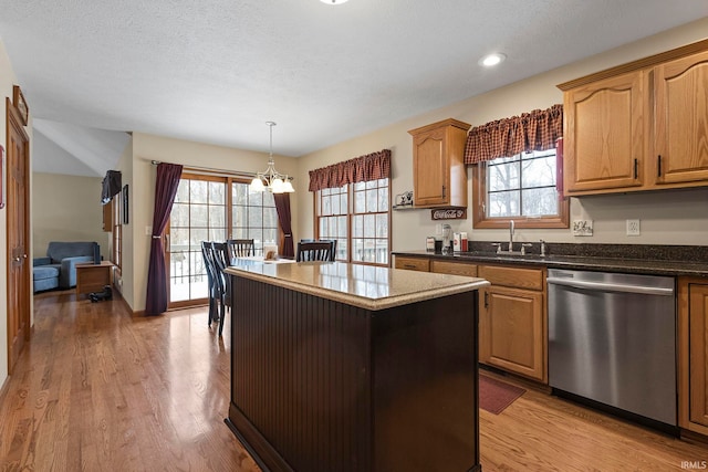 kitchen featuring sink, hanging light fixtures, a kitchen island, stainless steel dishwasher, and light wood-type flooring