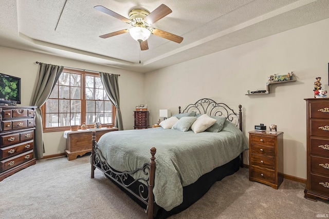 bedroom with ceiling fan, a raised ceiling, light colored carpet, and a textured ceiling