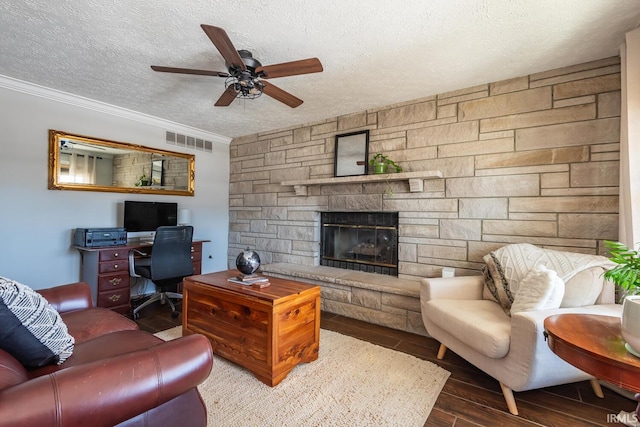 living room featuring ornamental molding, a stone fireplace, ceiling fan, and a textured ceiling