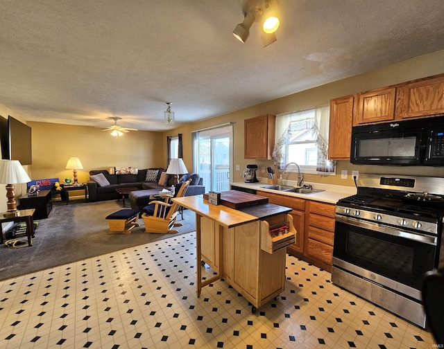 kitchen featuring a breakfast bar, sink, stainless steel gas range oven, a textured ceiling, and ceiling fan