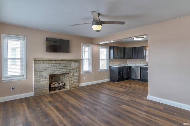 unfurnished living room featuring ceiling fan, dark hardwood / wood-style flooring, and a stone fireplace