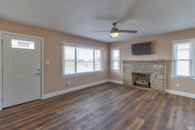 unfurnished living room with a stone fireplace, dark hardwood / wood-style floors, and ceiling fan