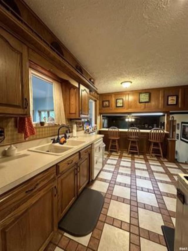 kitchen with sink, light tile patterned floors, a textured ceiling, and wood walls