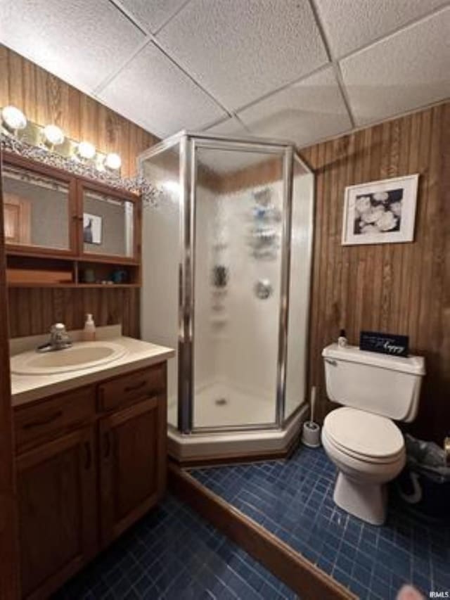 bathroom with a paneled ceiling, wooden walls, vanity, tile patterned floors, and walk in shower