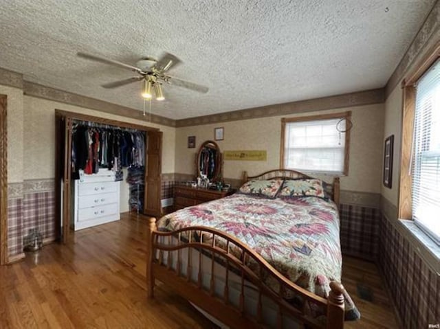 bedroom with multiple windows, a textured ceiling, wood-type flooring, and ceiling fan