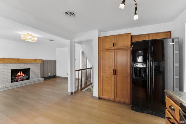 kitchen with a brick fireplace, black fridge with ice dispenser, and light hardwood / wood-style flooring