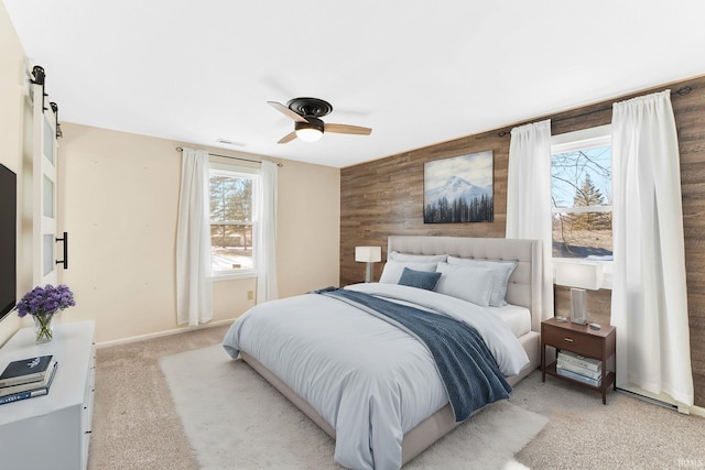 bedroom featuring multiple windows, ceiling fan, a barn door, and wooden walls