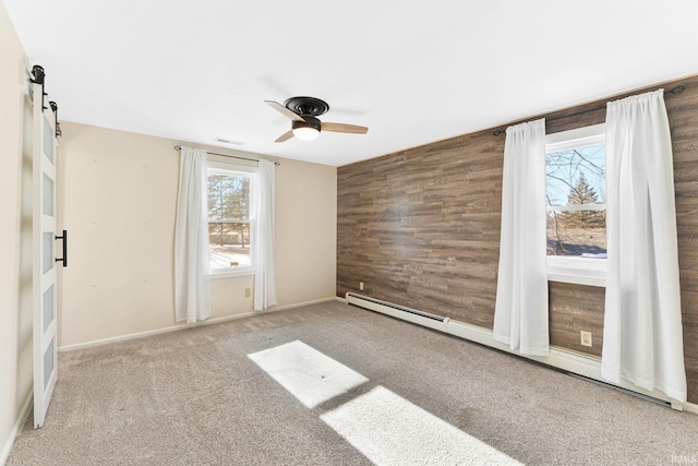 unfurnished room with light carpet, baseboard heating, wooden walls, ceiling fan, and a barn door