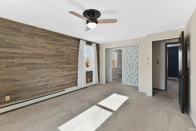 unfurnished bedroom featuring ceiling fan, carpet floors, wooden walls, and baseboard heating