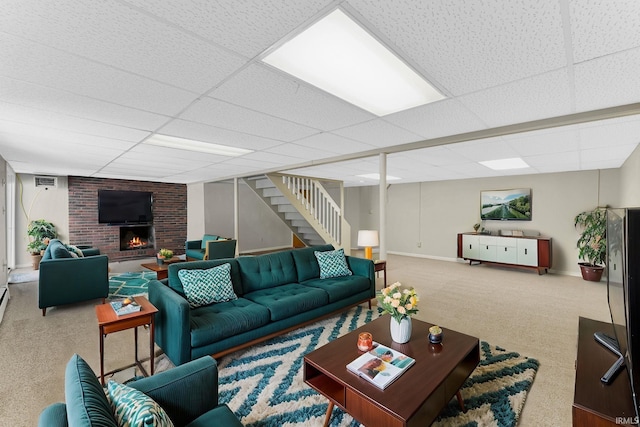 carpeted living room featuring a brick fireplace and a drop ceiling