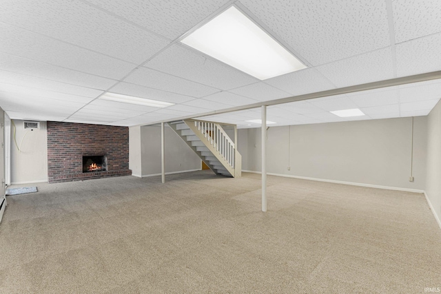 basement featuring carpet floors, a brick fireplace, and a drop ceiling