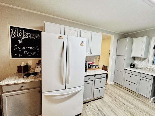 kitchen with light hardwood / wood-style flooring, white cabinetry, backsplash, ornamental molding, and white fridge