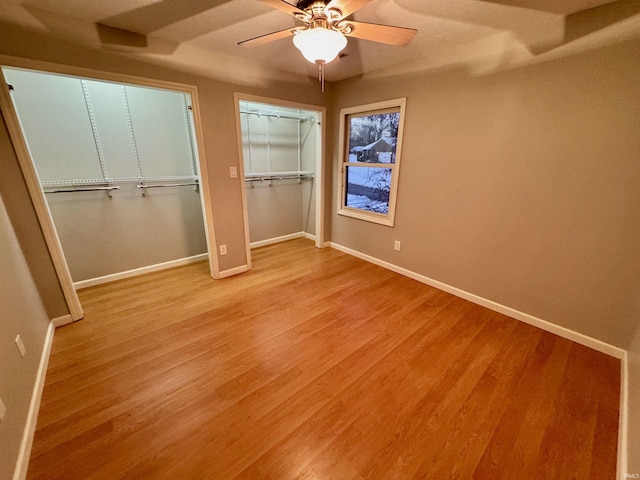 unfurnished bedroom with ceiling fan, two closets, and light hardwood / wood-style floors