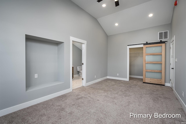 unfurnished bedroom with ensuite bath, a walk in closet, a closet, light colored carpet, and a barn door