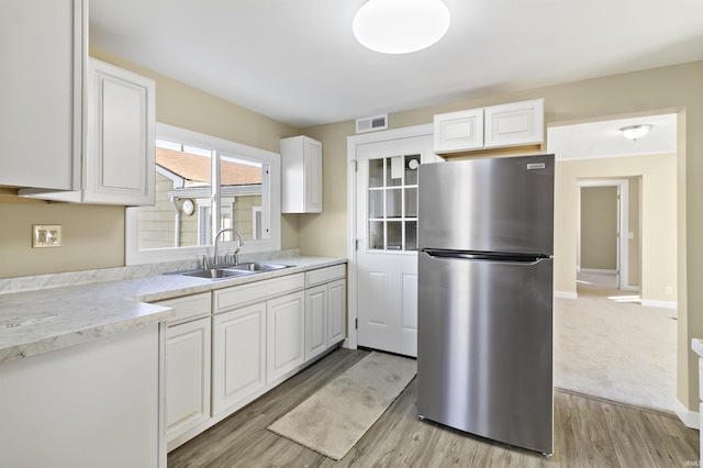 kitchen with stainless steel refrigerator, sink, white cabinets, light stone countertops, and light wood-type flooring