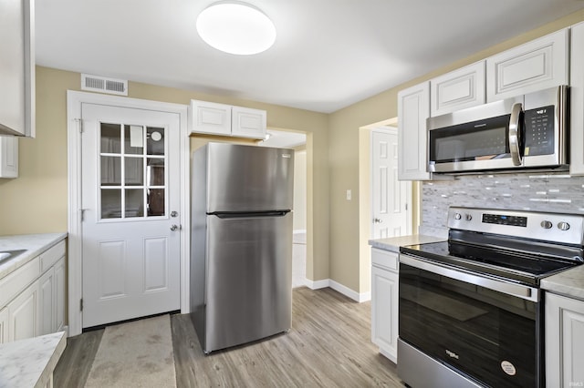 kitchen with decorative backsplash, light hardwood / wood-style flooring, white cabinets, and appliances with stainless steel finishes