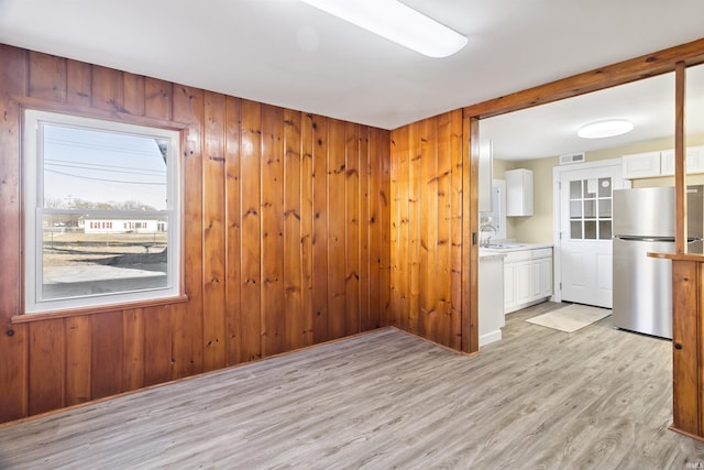 unfurnished room featuring sink, wood walls, and light hardwood / wood-style flooring