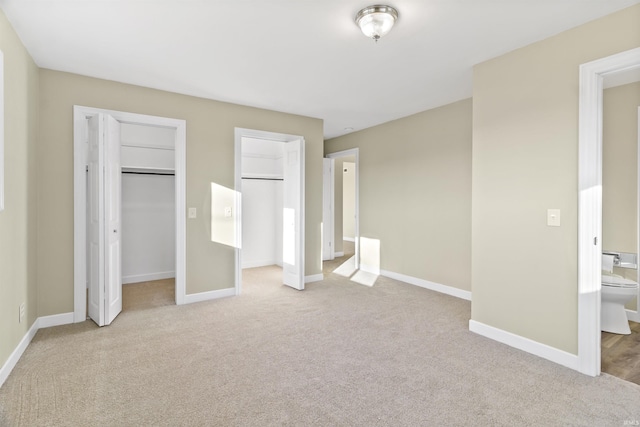 unfurnished bedroom featuring multiple closets, ensuite bathroom, and light colored carpet