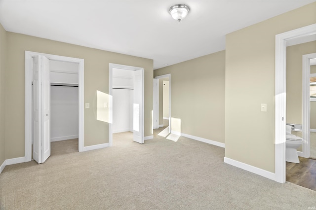 unfurnished bedroom with multiple closets, ensuite bath, and light carpet