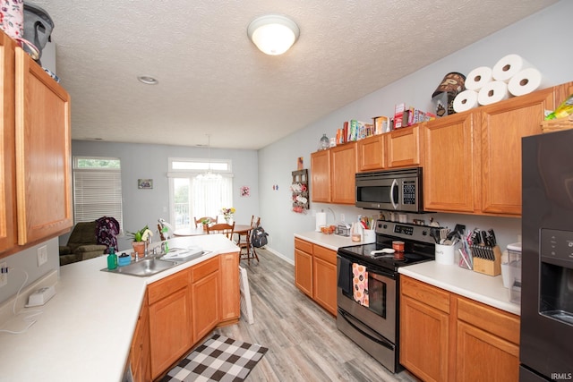 kitchen with appliances with stainless steel finishes, decorative light fixtures, sink, light hardwood / wood-style floors, and a textured ceiling