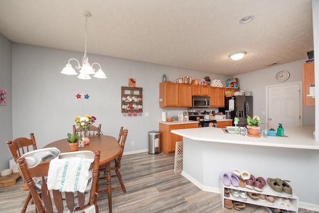 kitchen with pendant lighting, stainless steel appliances, a notable chandelier, light hardwood / wood-style floors, and a textured ceiling