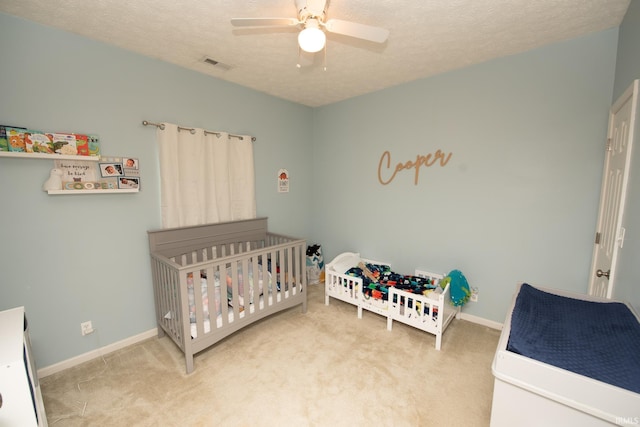 bedroom with a nursery area, ceiling fan, carpet, and a textured ceiling