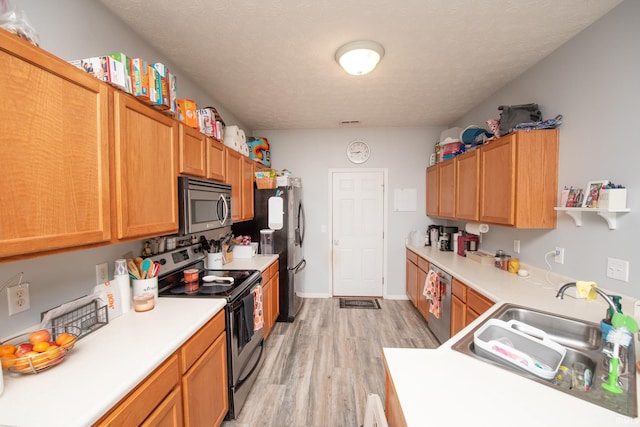 kitchen featuring stainless steel appliances, sink, a textured ceiling, and light wood-type flooring